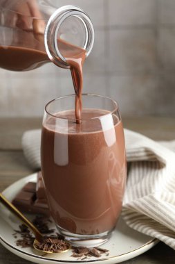 Tahta masada çikolatalı sütü bardağa dolduran kadın, yakın plan.