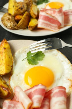 Tasty brunch. Fried egg, potato, bacon and fork on dark table, closeup
