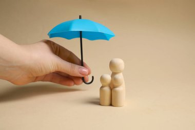 Bej arka planda insan figürlerinin üzerinde şemsiye tutan kadın, yakın plan. Sigorta konsepti