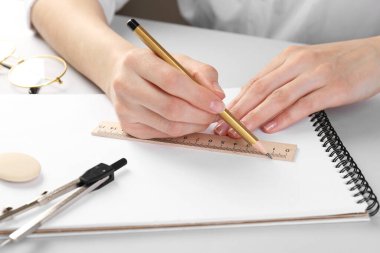 Beyaz masadaki deftere cetvel ve kalemle çizim yapan kadın, yakın plan.