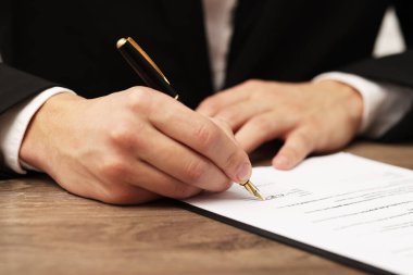 İçerideki ahşap masada, ruhsat sözleşmesi imzalayan adam, yakın plan.