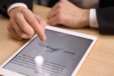 Elektronik imza. Ahşap masada tablet kullanan adam, yakın plan.
