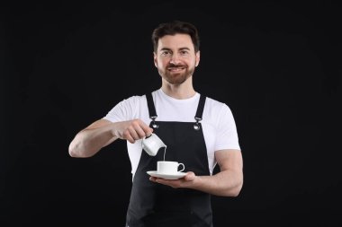 Gülümseyen barista siyah arka planda kahve yapıyor.