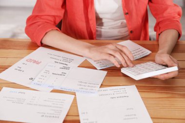 Faturaları ödüyorum. İçerideki ahşap masada hesap makinesi ve faturaları olan kadın.