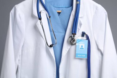 Steteskop ve rozetli doktorun ceketi gri arka planda, yakın plan.