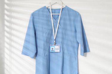 Beyaz duvara asılmış rozetli bir sağlık görevlisi üniforması.