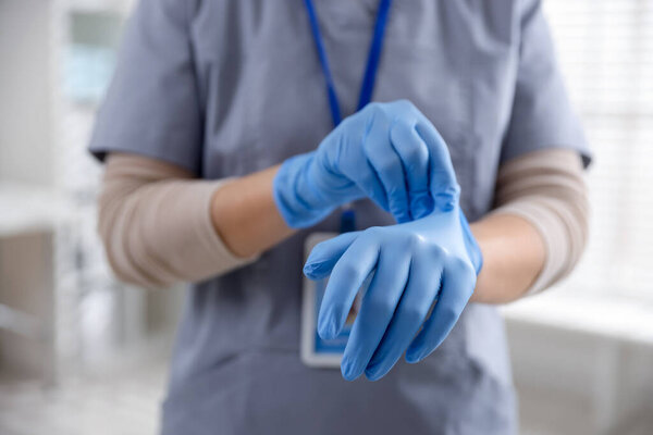 Medical worker putting on gloves in hospital, closeup