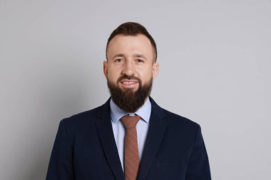 Gri arka planda takım elbiseli yakışıklı sakallı adam.