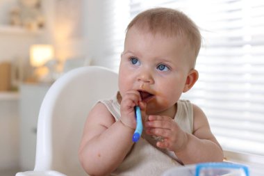 Evde kaşıkla yemek yiyen şirin bir bebek.