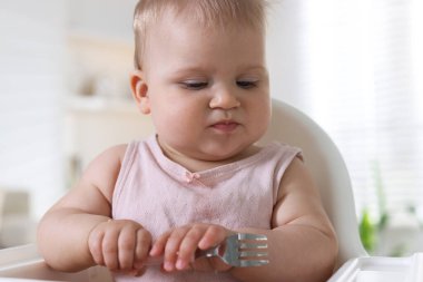 Evdeki beslenme sandalyesinde çatalla yemek yiyen şirin bir bebek.