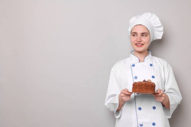 Üniformalı şekerci açık gri arka planda çikolatalı kek tutuyor, mesaj için yer var.