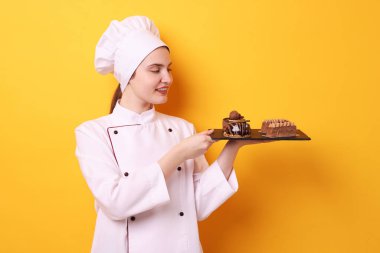 Üniformalı şekerlemecinin elinde turuncu arka planda lezzetli çikolatalı tatlılar var.