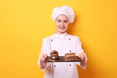 Üniformalı şekerlemecinin elinde turuncu arka planda lezzetli çikolatalı tatlılar var.