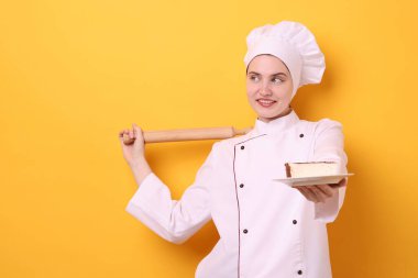 Üniformalı pastacı elinde oklavayla turuncu arka planda lezzetli bir pasta tutuyor. Mesaj için yer var.