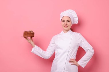 Üniformalı pastacı pembe arka planda lezzetli çikolatalı pasta tutuyor.