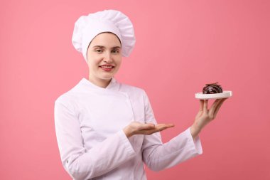 Üniformalı şekerci pembe arka planda çikolatalı tatlı tutuyor.