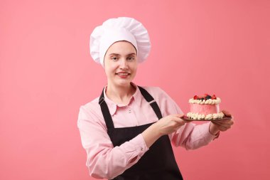 Şekerci pembe arka planda lezzetli bir pasta tutuyor.