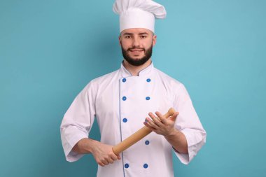 Üniformalı mutlu pastacı açık mavi arka planda merdane tutuyor.