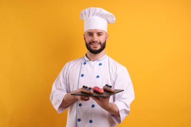 Üniformalı mutlu pastacı turuncu arka planda ekinler tutuyor.