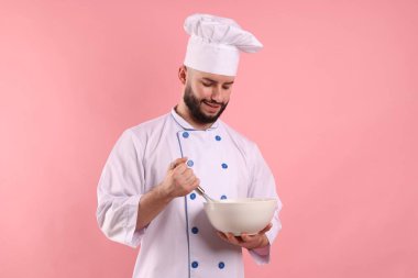 Pembe arka planda çırpı ve kase tutan üniformalı mutlu pastacı.