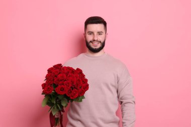 Pembe arka planda kırmızı güller açan mutlu bir adam.