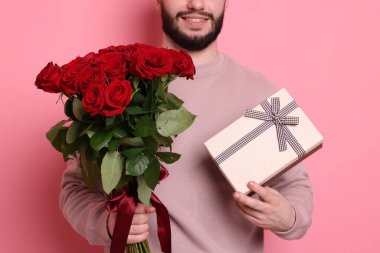Kırmızı gül buketi ve pembe arka planda hediye kutusu olan adam, yakın plan.