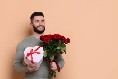 Kırmızı gül buketi ve bej arka planda hediye kutusu olan mutlu adam, mesaj için yer var.