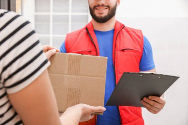 Gülümseyen kurye pano ile kapalı alandaki alıcıya paket veriyor, yakın plan