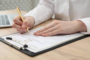 Klinikteki ahşap masada sağlık sigortası poliçesi dolduran doktor.