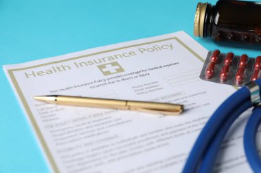 Sağlık sigortası poliçesi, açık mavi arka planda kalem ve haplar, yakın plan