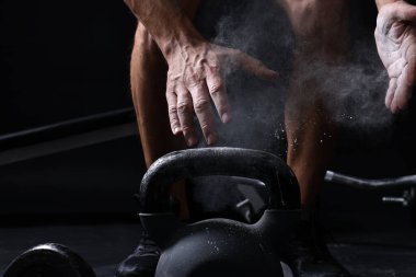 Siyah arka planda kettlebell eğitimi almadan önce talk pudrasıyla el çırpan adam, yakın plan.