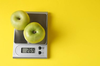 Elektronik mutfak terazisi, sarı arka planda elmalar, üst manzara. Metin için boşluk