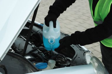 Plastik kutudan araba deposuna cam temizleyici döken bir adam var.