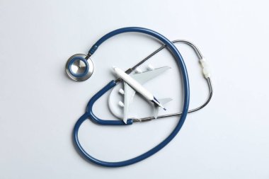 Tıbbi turizm. Açık gri zemin üzerinde stetoskop ve uçak modeli, düz yatıyordu