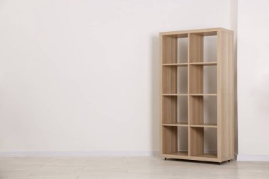Empty wooden shelving unit near white wall indoors, space for text