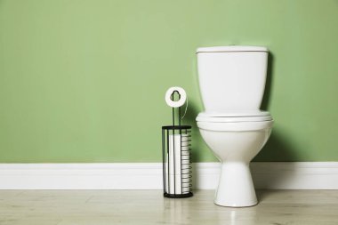 Yeşil duvarın yanında seramik klozet ve kağıt var.