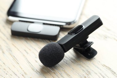 Lavalier mikrofon ve ahşap masada kablosuz alıcısı olan akıllı telefon.