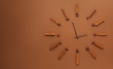 Tarçın çubukları, anason yıldızları ve kahverengi arka planda saati temsil eden vanilya kapsülleri, düz bir zemin. Metin için boşluk