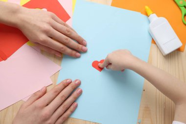 Anne ve kızı ahşap masada el yapımı tebrik kartı yapıyorlar.