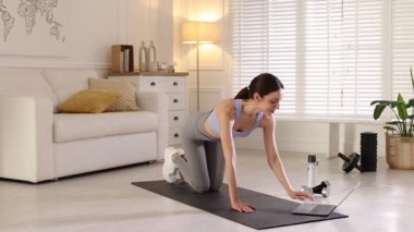 Evde dizüstü bilgisayarla video öğretirken egzersiz yapan kadın.