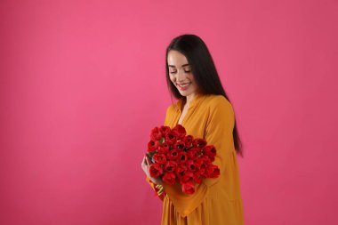 Pembe arka planda kırmızı lale buketi olan mutlu bir kadın. Mesaj için yer var. 8 Mart kutlamaları