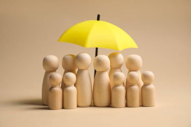 Bej arka planda şemsiye altında insan figürleri. Sigorta konsepti