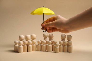 Bej arka planda insan figürlerinin üzerinde şemsiye tutan kadın, yakın plan. Sigorta konsepti
