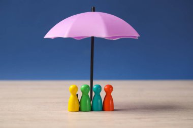 Şemsiyenin altındaki insan figürleri mavi arka plana karşı açık ahşap masa üzerinde. Sigorta konsepti