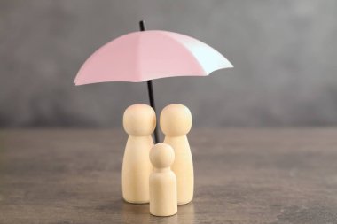 Gri masada şemsiye altındaki insan figürleri. Sigorta konsepti