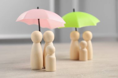 Şemsiyelerin altındaki insan figürleri açık ahşap masa üzerinde, seçici bir odak. Sigorta konsepti