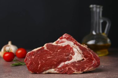 One piece of raw beef on brown textured table against black background, closeup