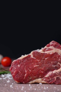 Bir parça çiğ sığır eti, kahverengi desenli bir masada siyah arka planda, yakın plan. Metin için boşluk