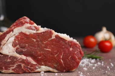 One piece of raw beef with salt on brown textured table against black background, closeup
