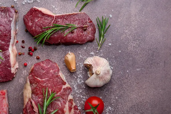 Kahverengi desenli masa üzerinde çiğ sığır eti, baharat ve ürünlerle bezenmiş düz bir kompozisyon. Metin için boşluk